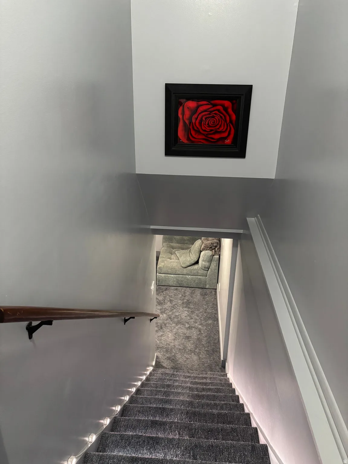Stairwell featuring gray carpeting, white painted walls, and a wooden handrail with black brackets