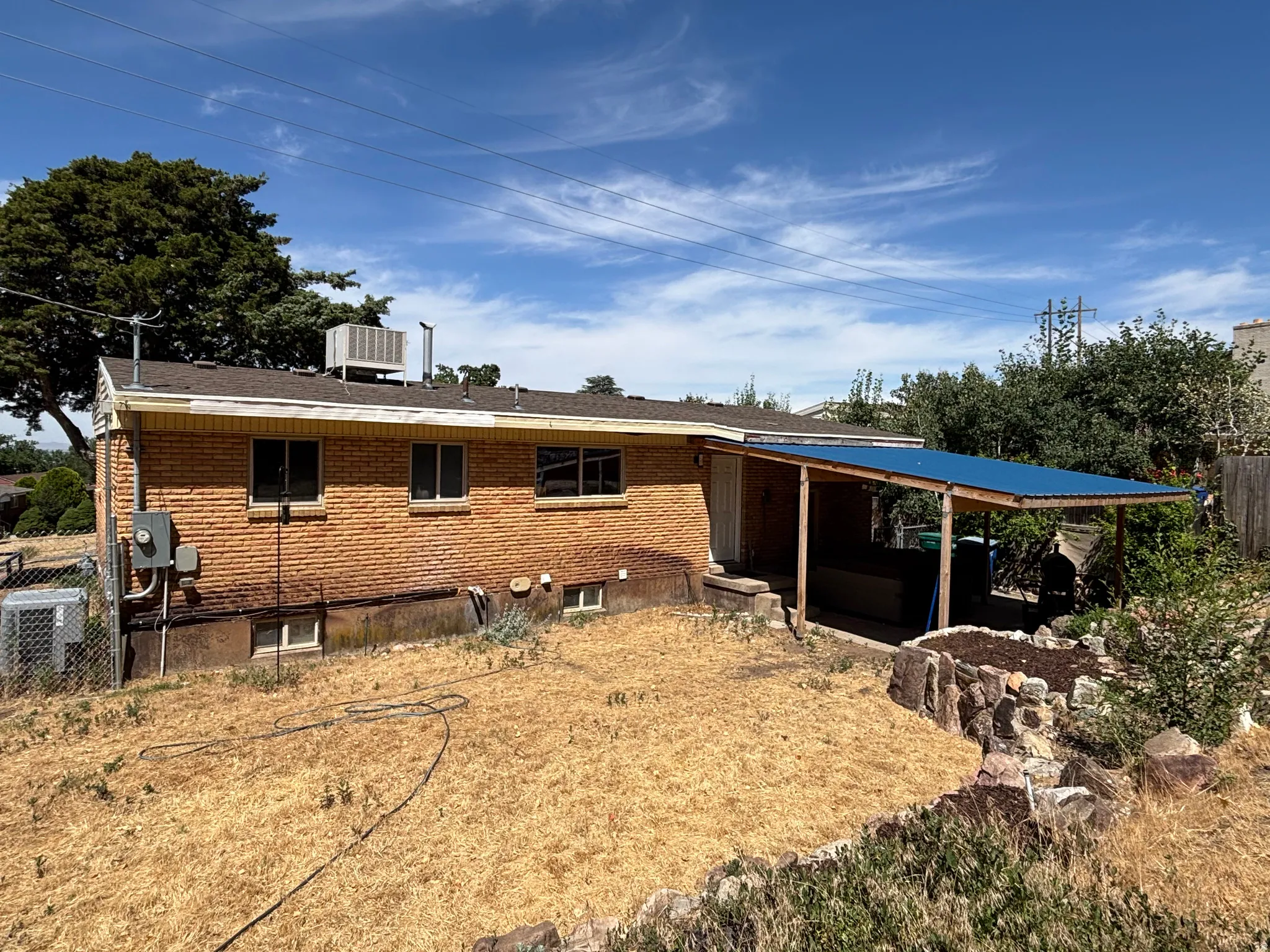 Brick exterior with multiple windows and a covered patio featuring a blue corrugated roof