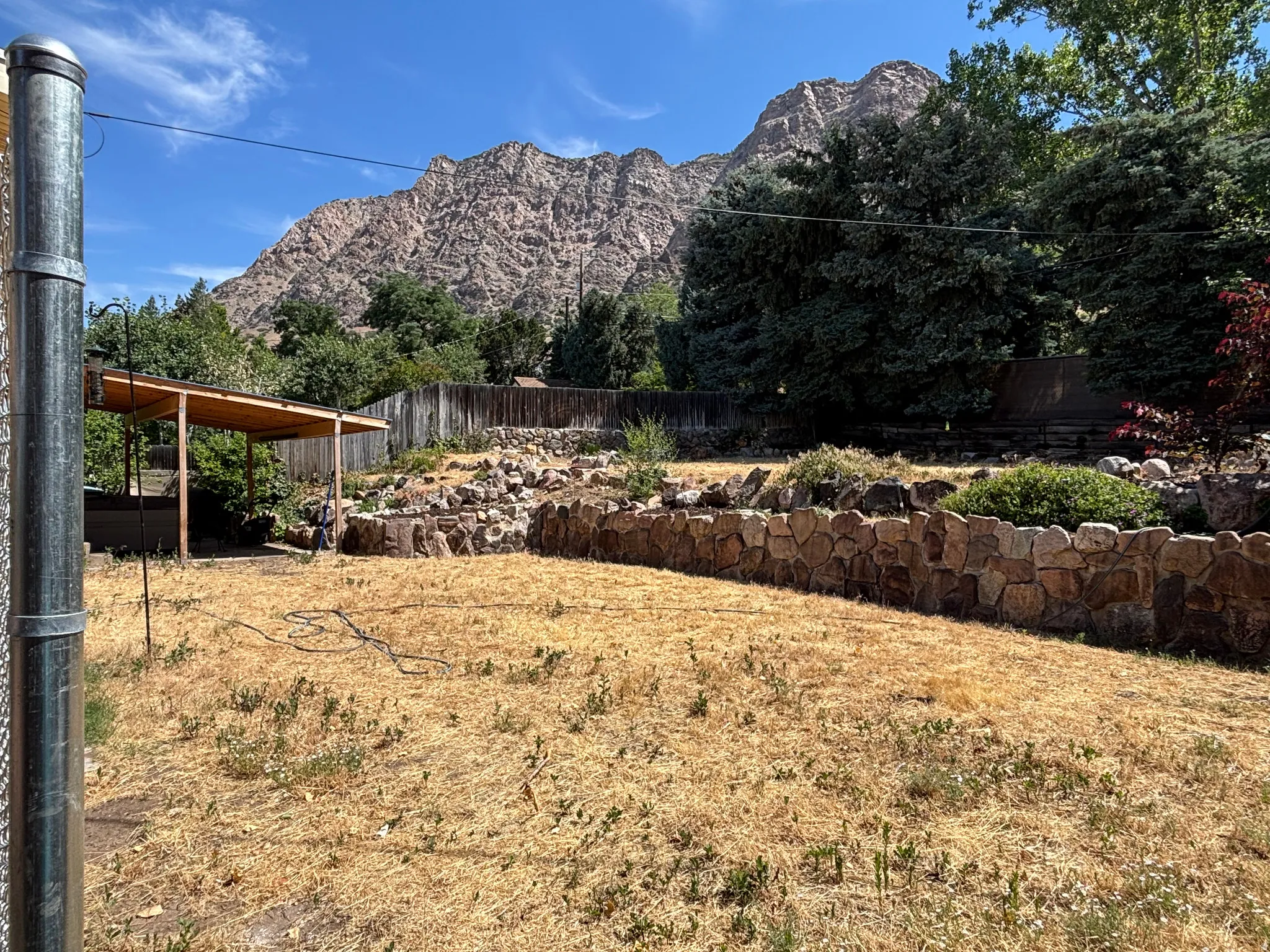 Expansive backyard with a stone retaining wall, mature trees, and a mountain backdrop