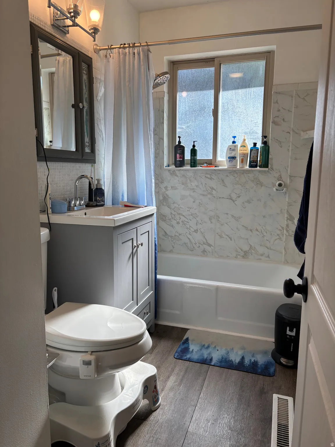 Bathroom featuring a white bathtub, white marble-patterned wall surround, and a chrome shower head