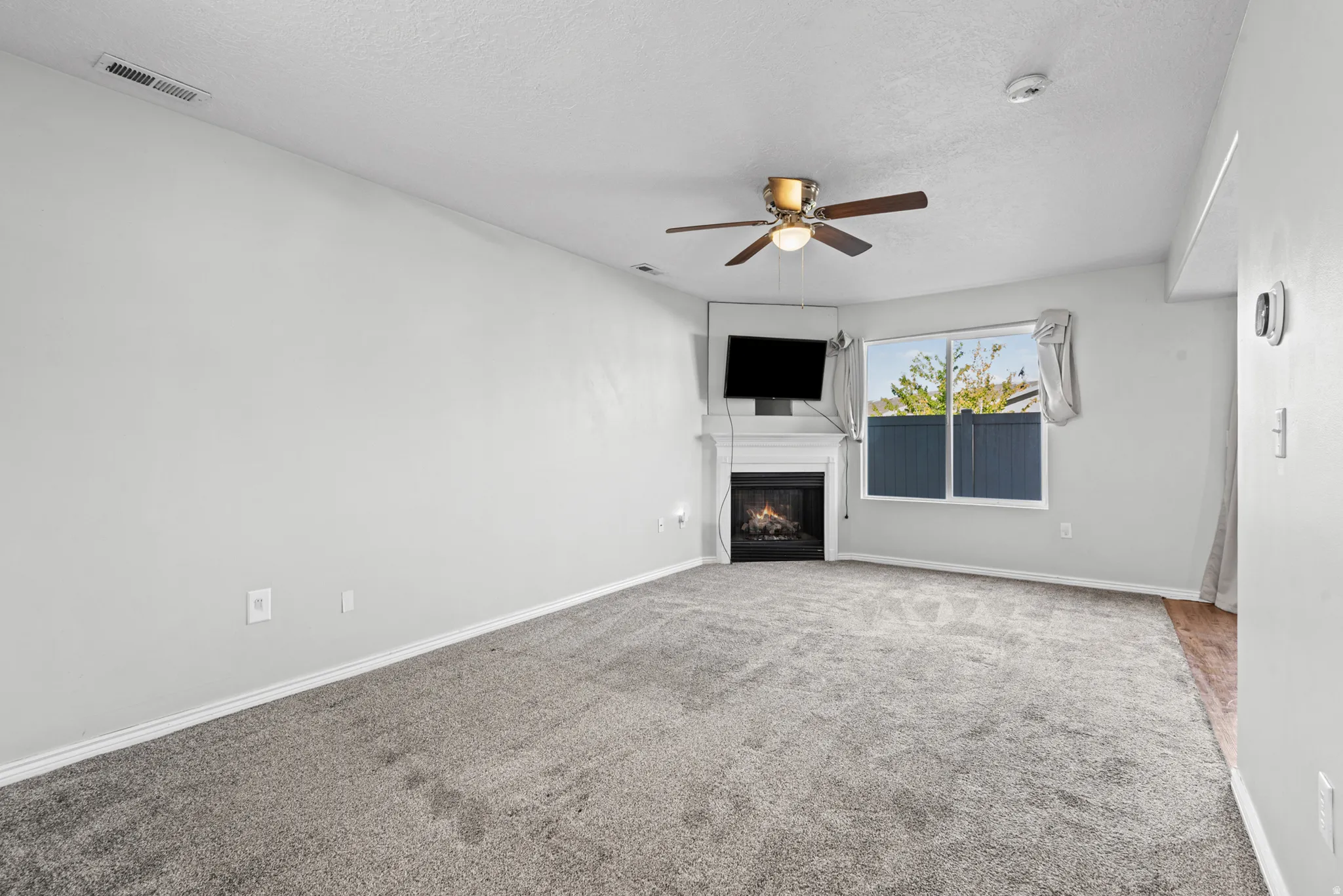 Living area featuring neutral-toned carpet, a corner fireplace with a white mantel, and a ceiling fan with integrated lighting