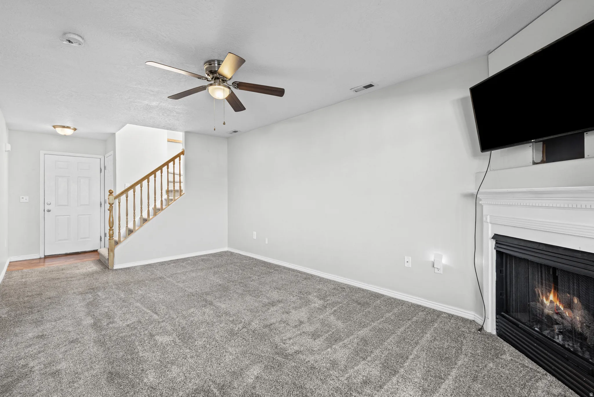 Living area featuring gray carpeting, a fireplace with a white mantel, and a ceiling fan with integrated lighting