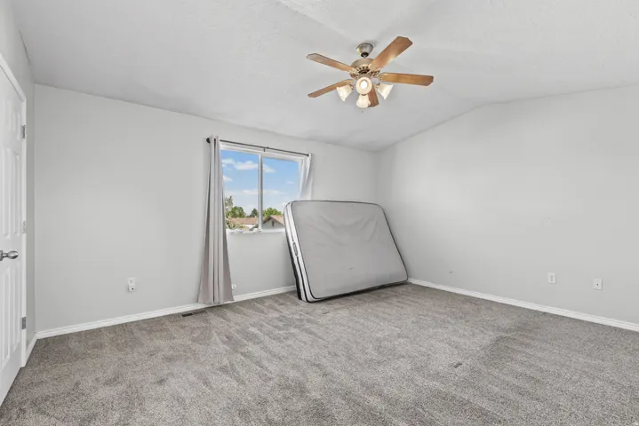 Carpeted room featuring a ceiling fan with integrated lighting, a window with curtains, and a paneled door