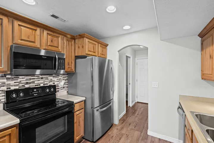 Kitchen featuring wood cabinetry, stainless steel appliances, mosaic tile backsplash, wood-finish flooring, and recessed lighting