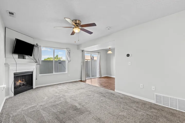 Living area featuring gray carpet, a fireplace with a white mantel, and a ceiling fan with integrated lighting