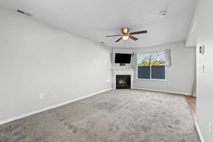 Living area featuring neutral-toned carpet, a corner fireplace with a white mantel, and a ceiling fan with integrated lighting