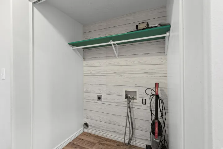 Utility closet featuring wood-finish flooring, shiplap-style wall paneling, and a mounted storage shelf