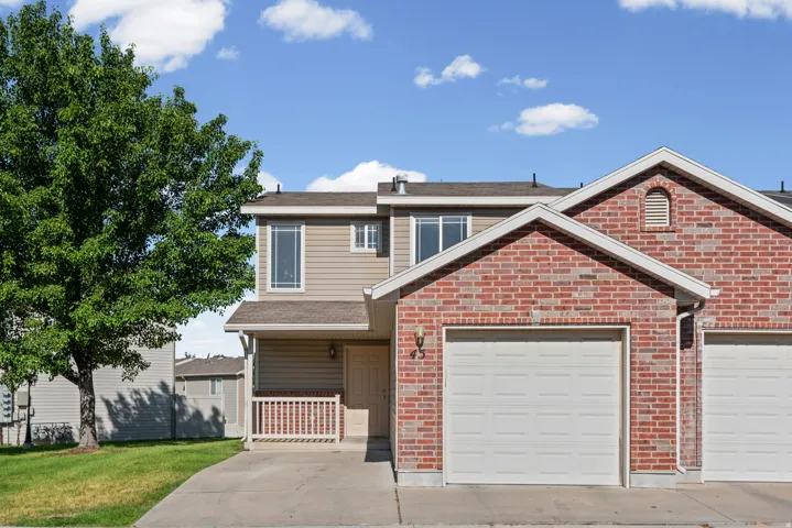 Brick and siding exterior featuring an attached garage, covered front porch with white railing, and a mature tree