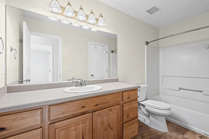 Bathroom featuring a wood-finish vanity with a light-toned countertop, an integrated sink, a large wall-mounted mirror, and a combined tub and shower unit