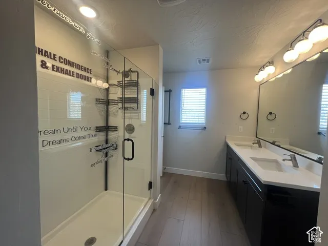 Spacious bathroom featuring a glass-enclosed shower with white subway tile, a double vanity with white countertops, and wood-finish flooring