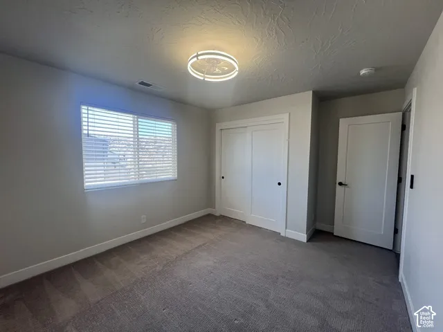 Carpeted room featuring a large window with blinds, a modern circular ceiling light fixture, a built-in closet with sliding doors, and a paneled interior door