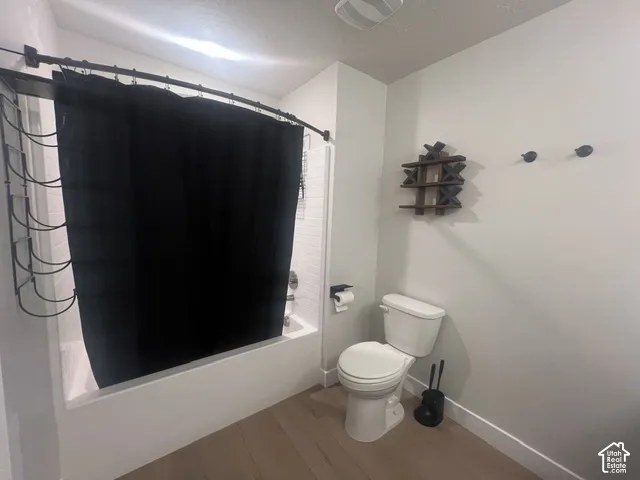 Bathroom featuring a tub/shower combination with white subway tile surround, wood-finish flooring, and a white toilet
