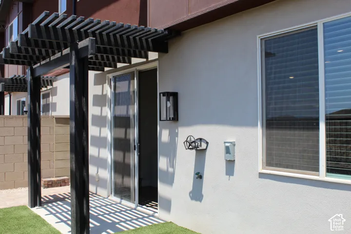 Outdoor patio area featuring a dark-stained wood pergola, sliding glass door, exterior wall sconce, and artificial turf