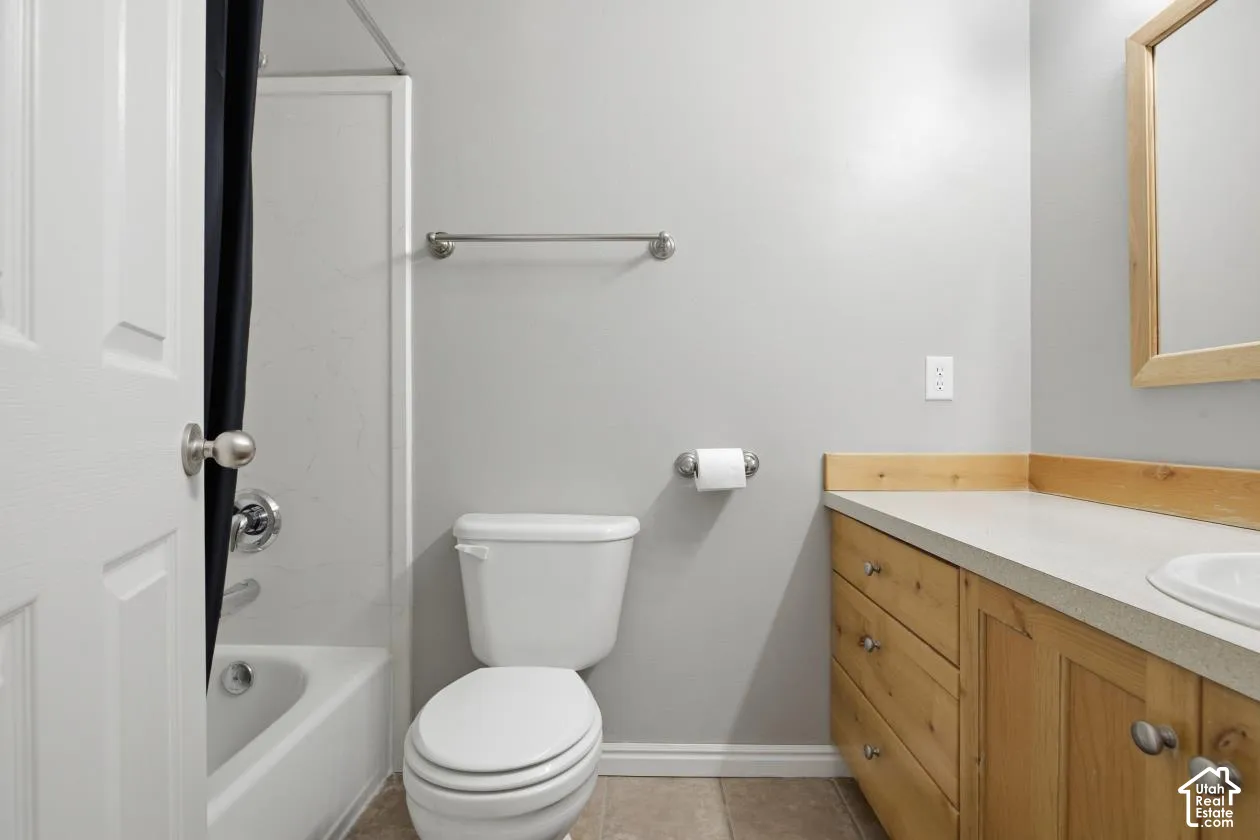 Bathroom featuring a white toilet, light wood-finish vanity with a light countertop, integrated sink, and a shower-tub combination with white subway tile surround