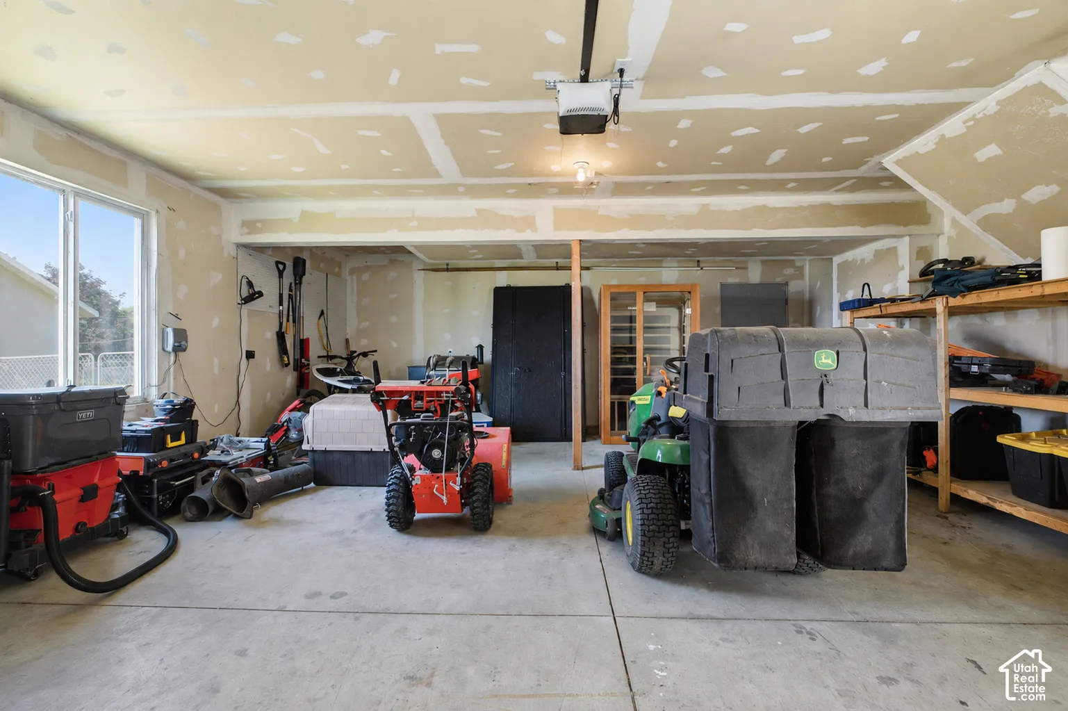 Spacious garage with concrete flooring, multiple windows, exposed drywall, an overhead garage door opener, and built-in shelving