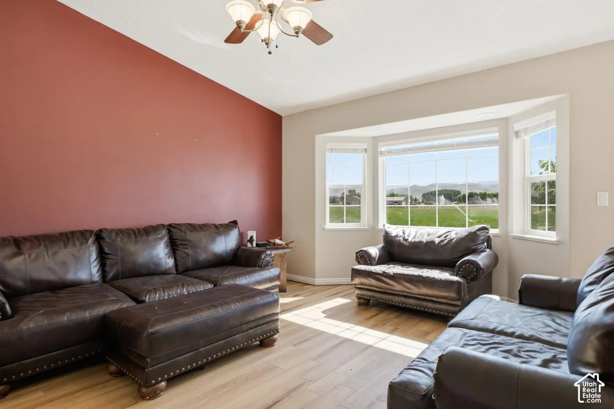 Bay window offering extensive exterior views, wood-finish flooring, vaulted ceiling with ceiling fan, and a prominent accent wall