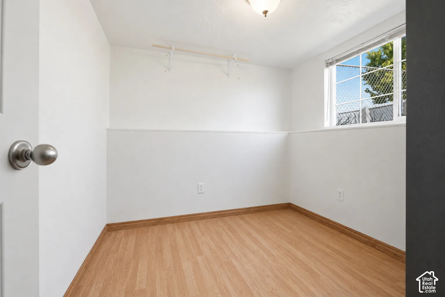 Room featuring wood-finish flooring, white painted walls, a window with exterior tree visibility, and a ceiling-mounted light fixture