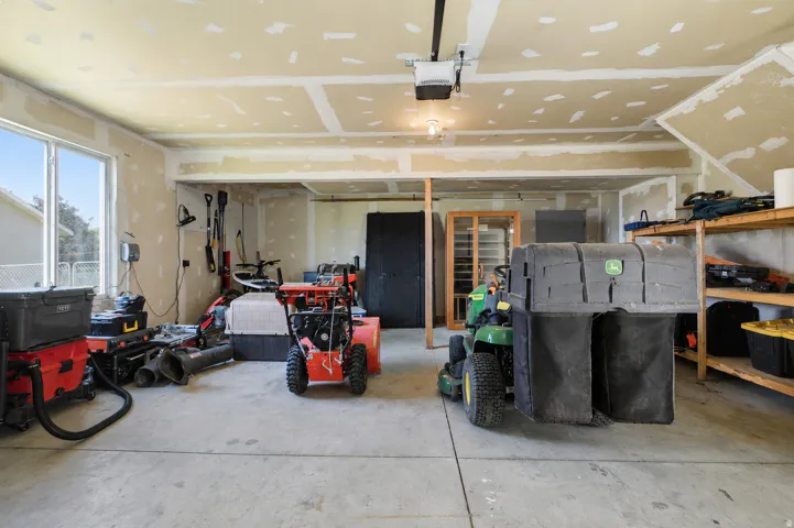 Spacious garage with concrete flooring, multiple windows, exposed drywall, an overhead garage door opener, and built-in shelving
