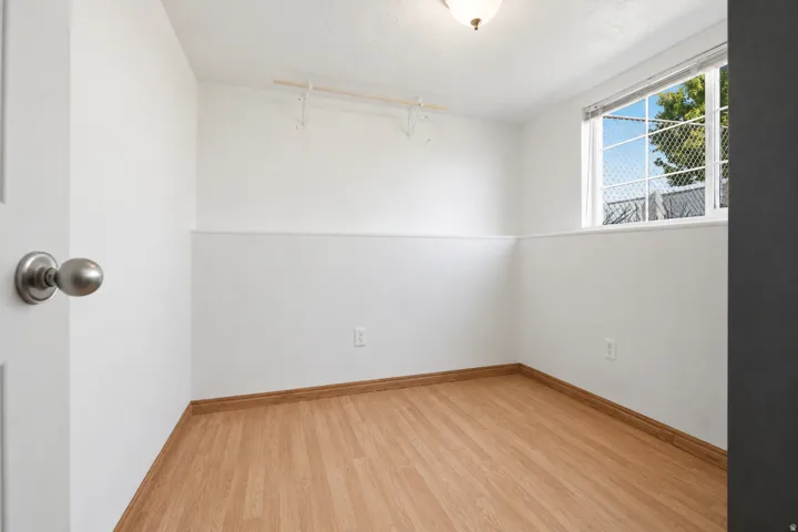 Room featuring wood-finish flooring, white painted walls, a window with exterior tree visibility, and a ceiling-mounted light fixture