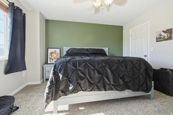 Carpeted room featuring a window with dark curtains, a ceiling fan with integrated lighting, a contrasting accent wall, and a white paneled door