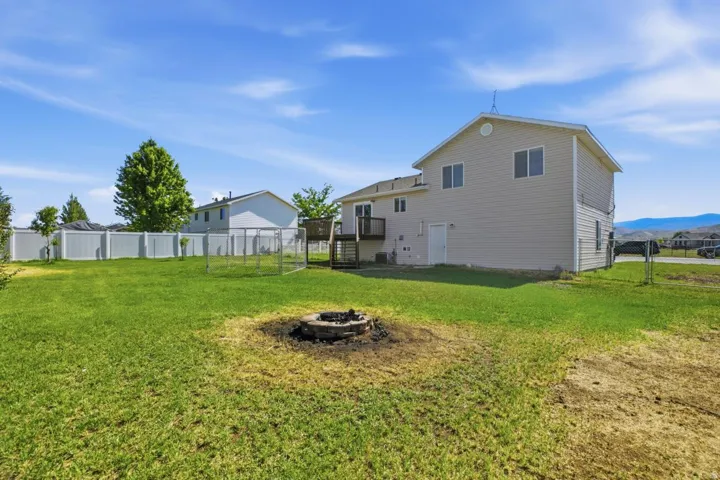 Expansive backyard featuring a built-in fire pit, a white vinyl privacy fence, and a chain-link enclosure