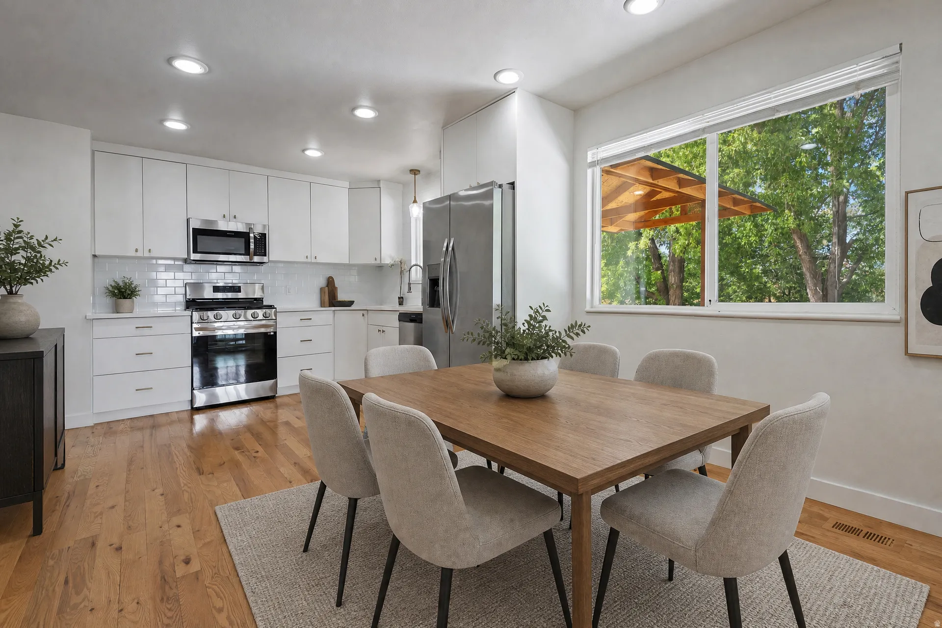 Eat-in kitchen featuring wood-finish flooring, white cabinetry, stainless steel appliances, a subway tile backsplash, and recessed lighting