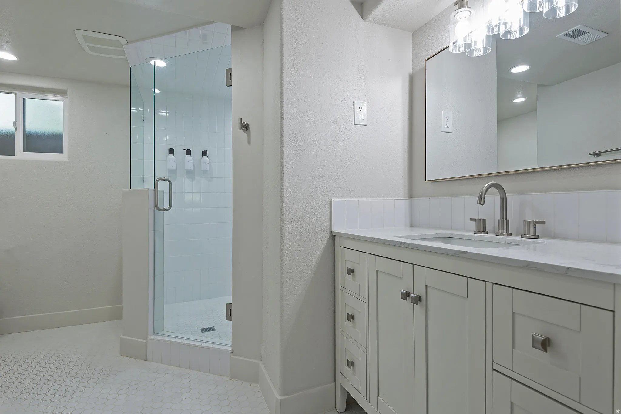 Modern bathroom featuring a glass-enclosed shower with white subway tile, a vanity with a white countertop and undermount sink, and hexagonal tile flooring