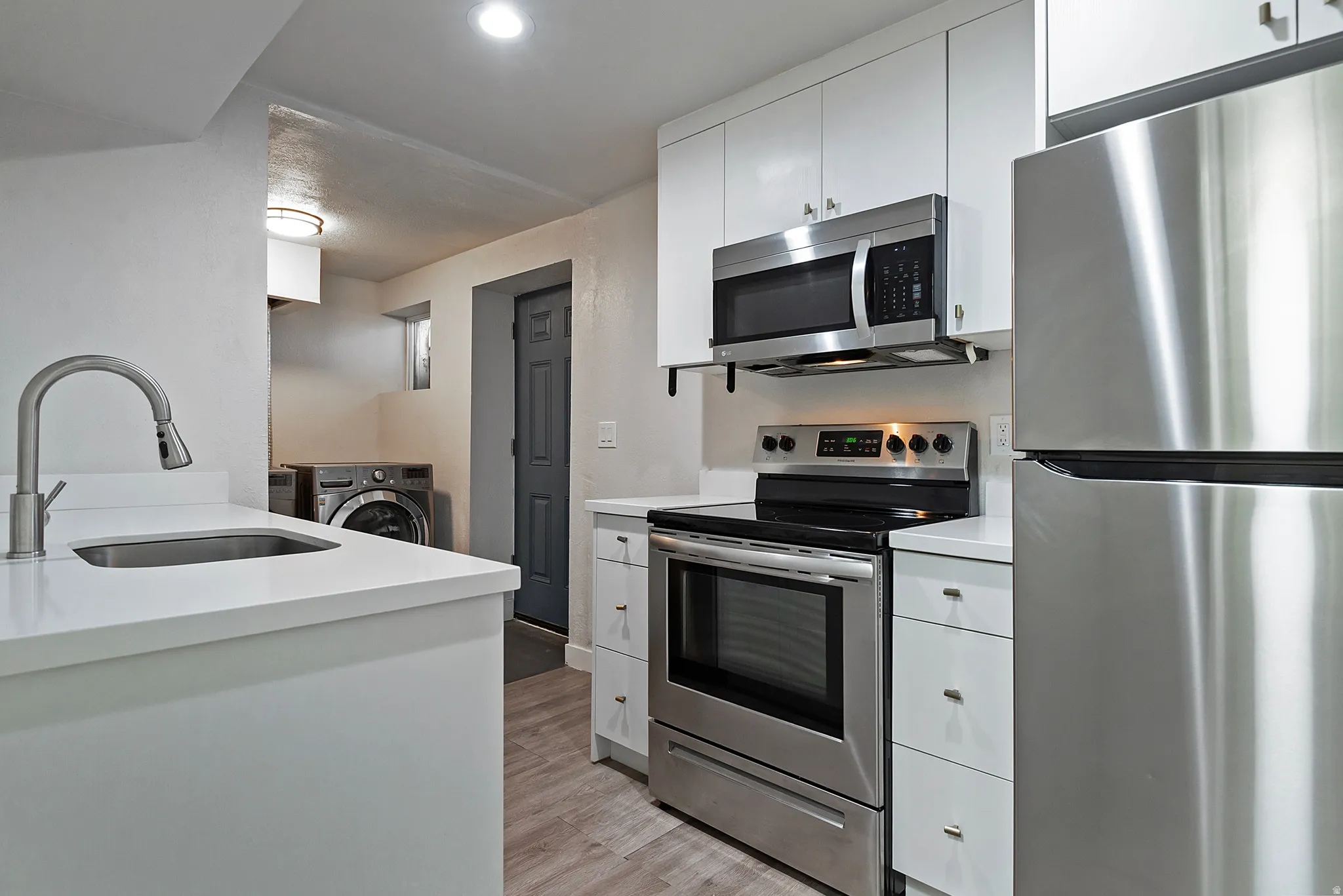 Modern kitchen featuring white cabinetry, stainless steel appliances, a stainless steel sink with a pull-down faucet, white countertops, and wood-finish flooring