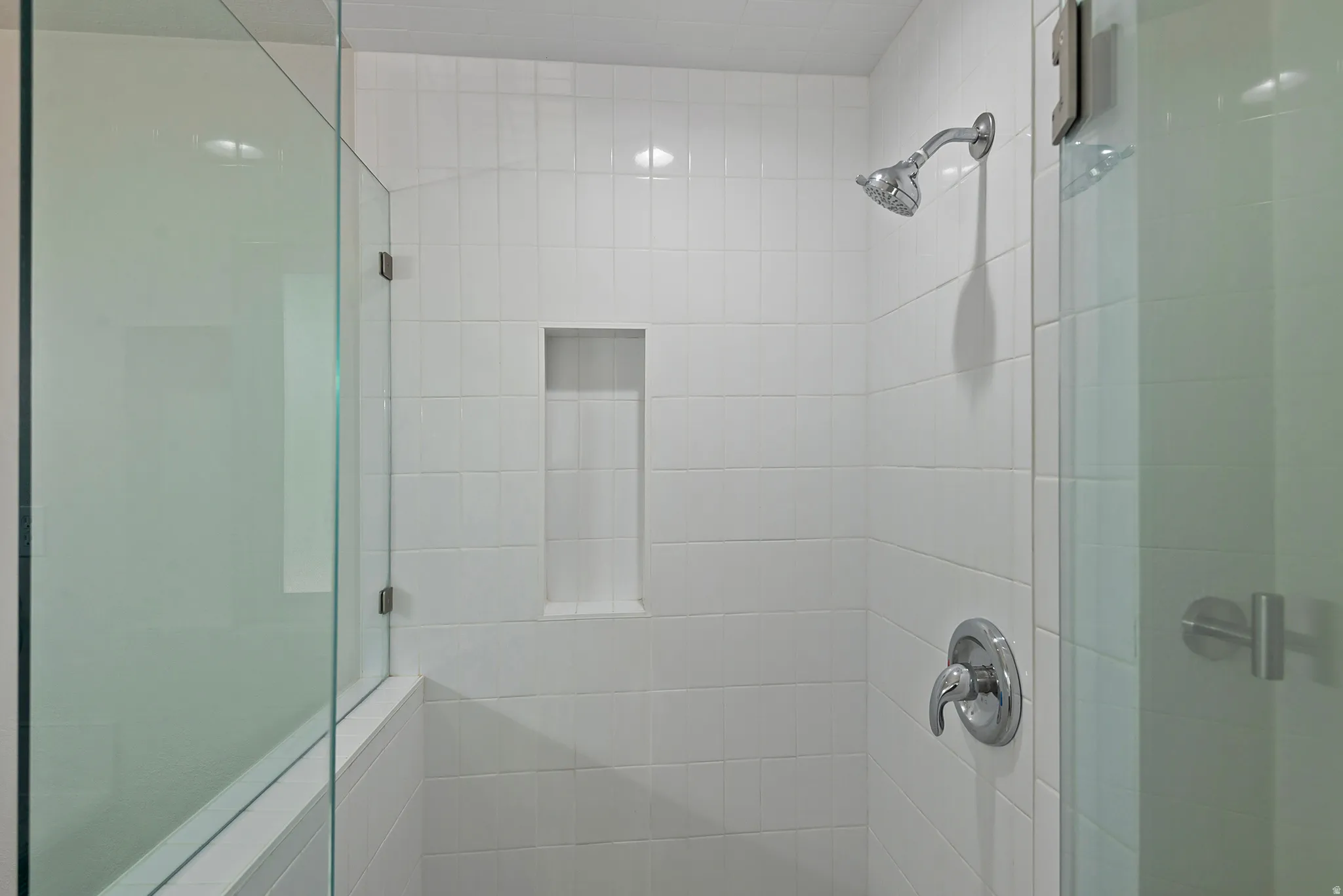 Shower enclosure featuring white subway tile, a built-in niche, and a glass partition