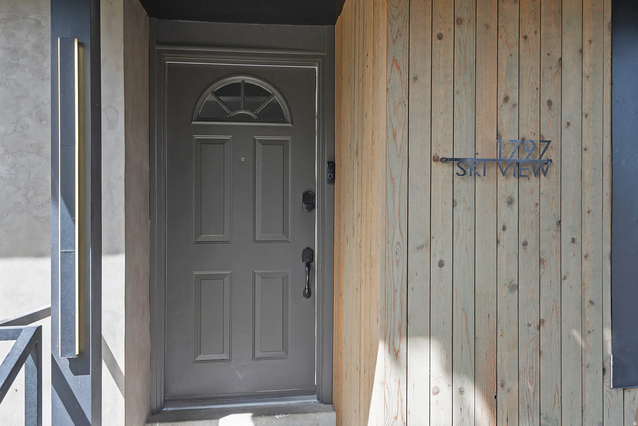 Entryway featuring a paneled door with an arched transom, vertical wood siding, and a modern exterior light fixture