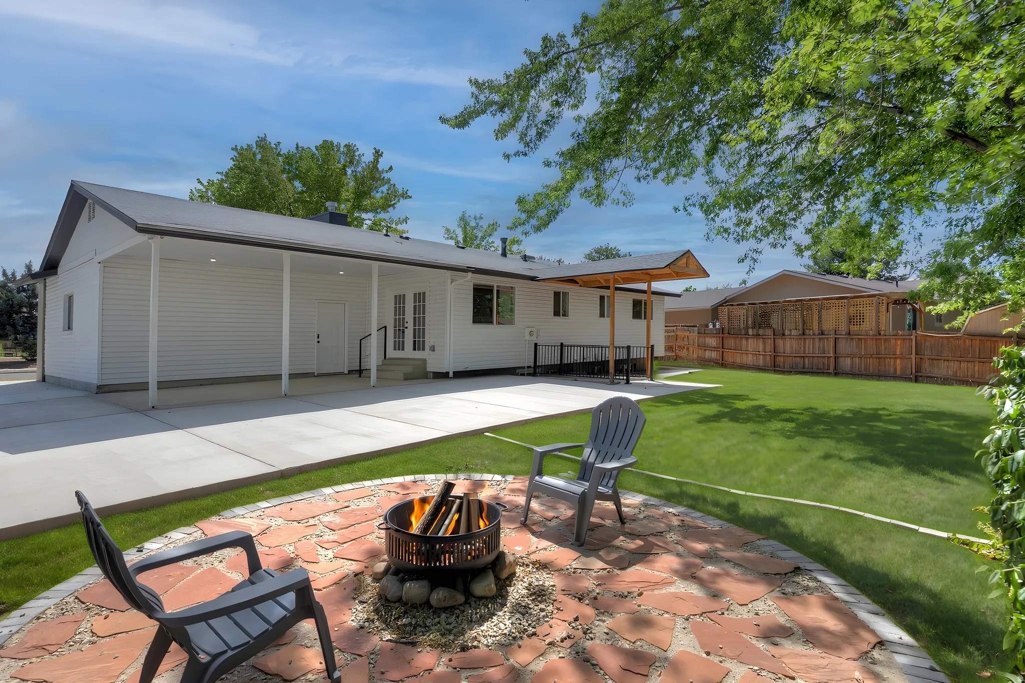 Expansive backyard featuring a large green lawn, flagstone patio with fire pit, covered patio with recessed lighting, and a secondary covered patio area