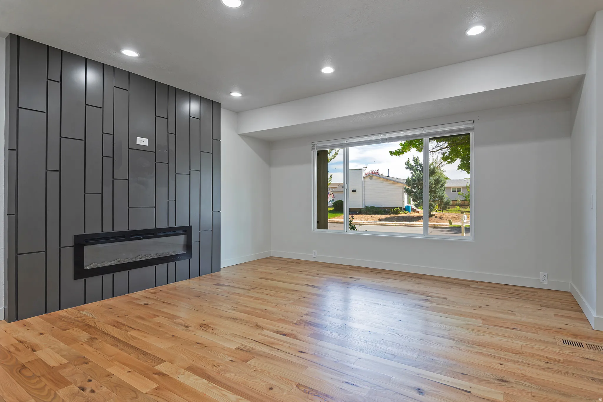 Wood-finish flooring and a contemporary linear fireplace are featured in this spacious room