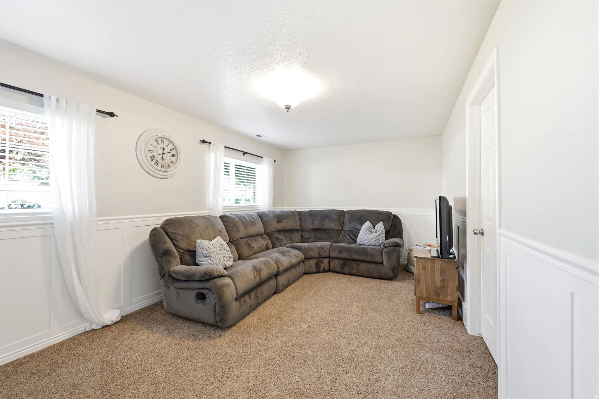 Spacious room featuring neutral carpet flooring, wainscoting, multiple windows with blinds, and recessed lighting