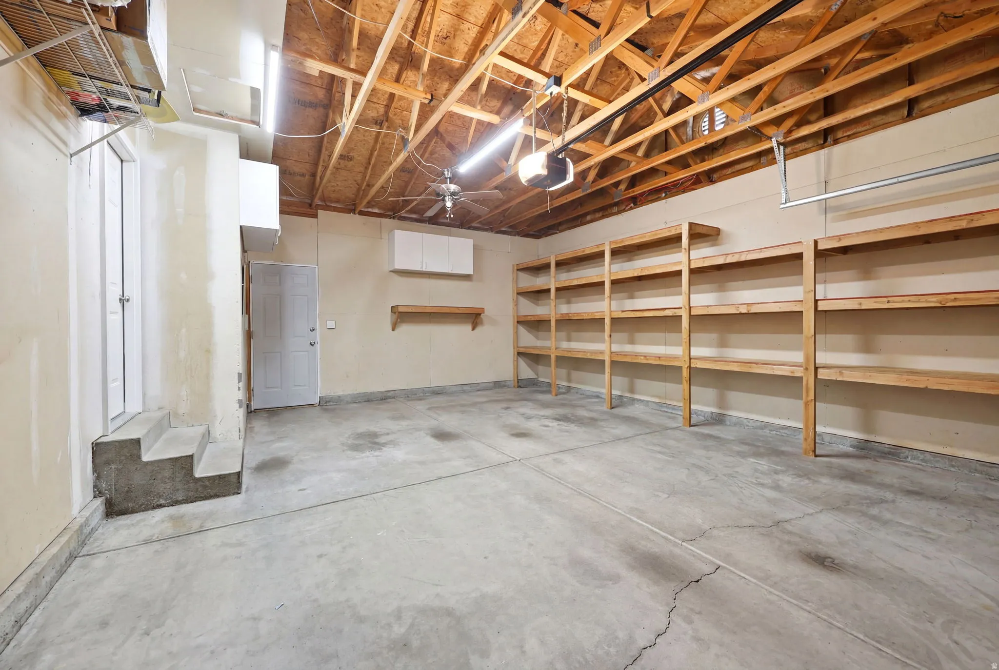 Spacious garage featuring a concrete floor, exposed wood beam ceiling, and extensive built-in shelving
