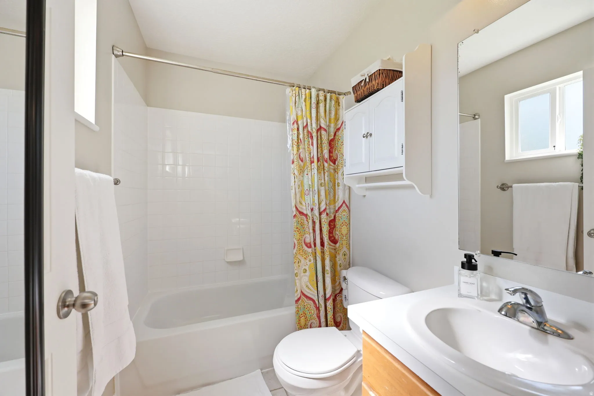 Full bathroom featuring a white tub-shower combination with subway tile surround, a single vanity with wood-finish cabinetry, and a mirrored wall cabinet