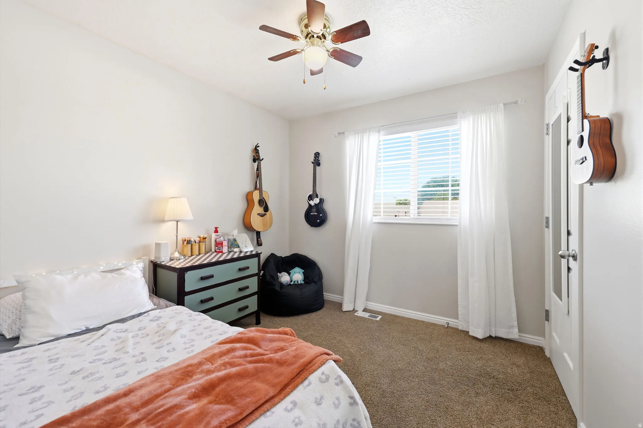 Carpeted room with a ceiling fan light fixture, a window with horizontal blinds and sheer white curtains, and white baseboards