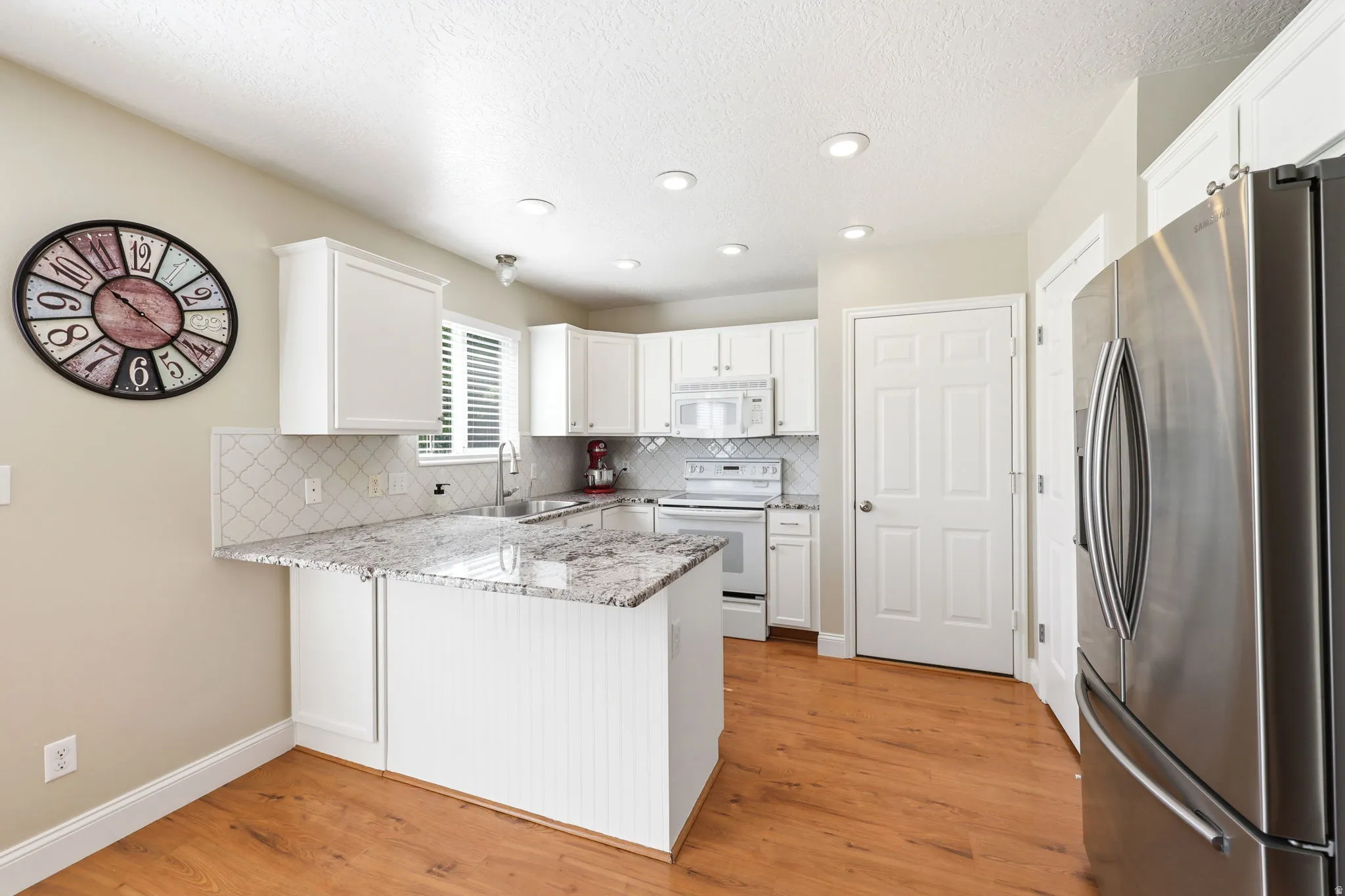 Kitchen featuring white cabinetry, light-toned countertops, a diagonal tile backsplash, stainless steel appliances, and recessed lighting
