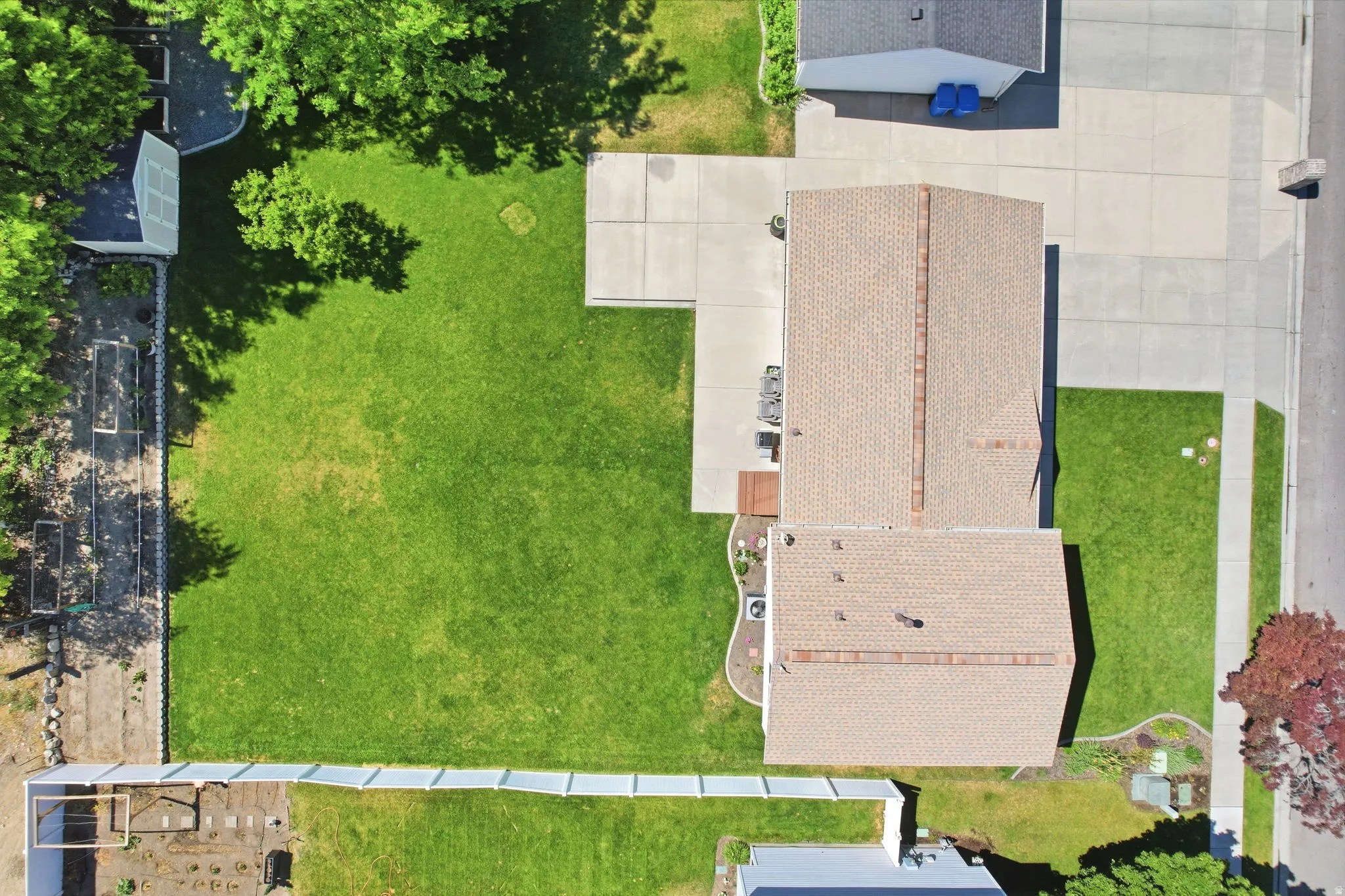 Expansive backyard featuring a lush lawn, concrete patio, white perimeter fencing, and raised garden beds
