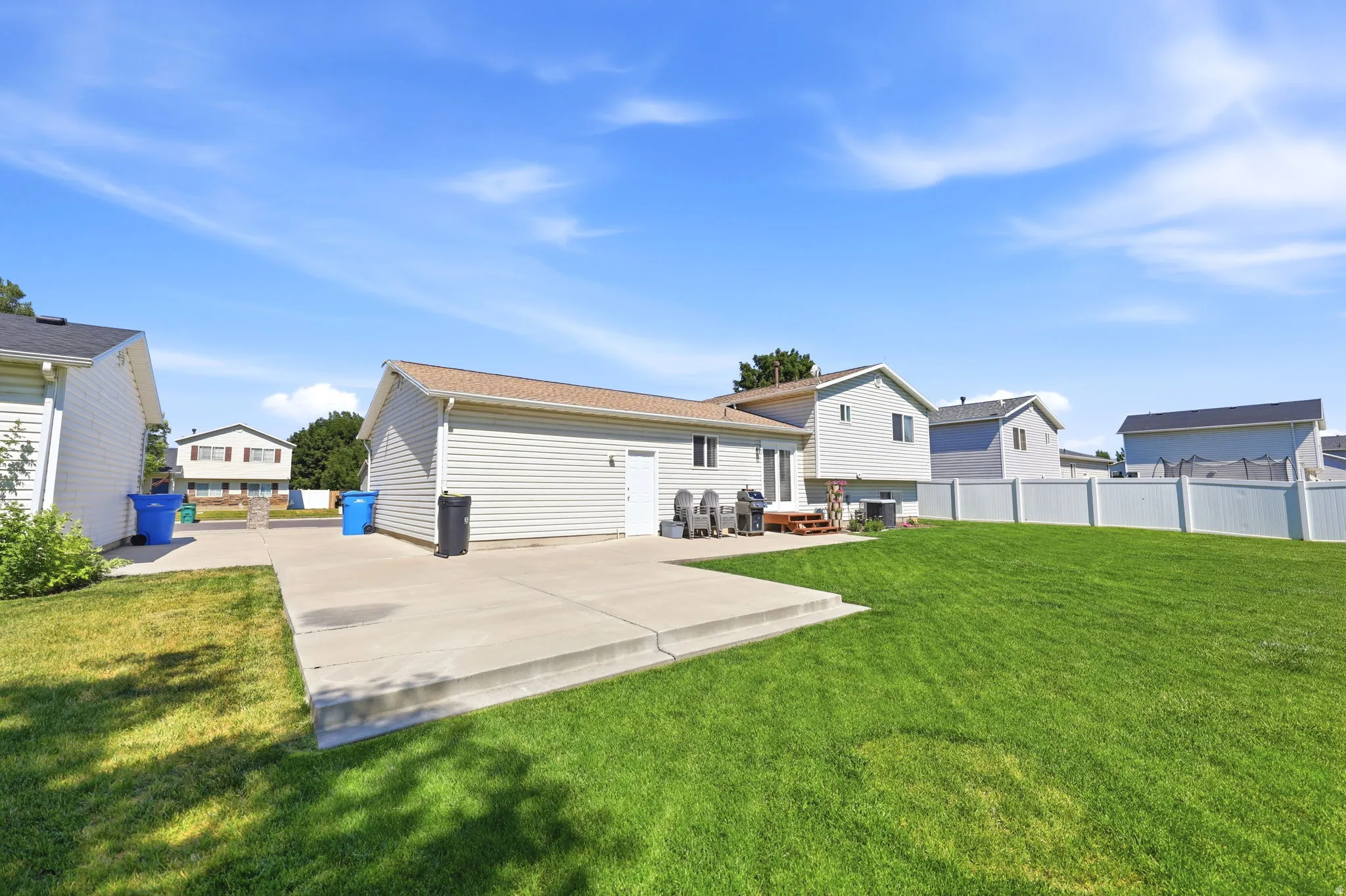 Expansive rear yard featuring a large concrete patio, a substantial lawn, and a light-colored privacy fence