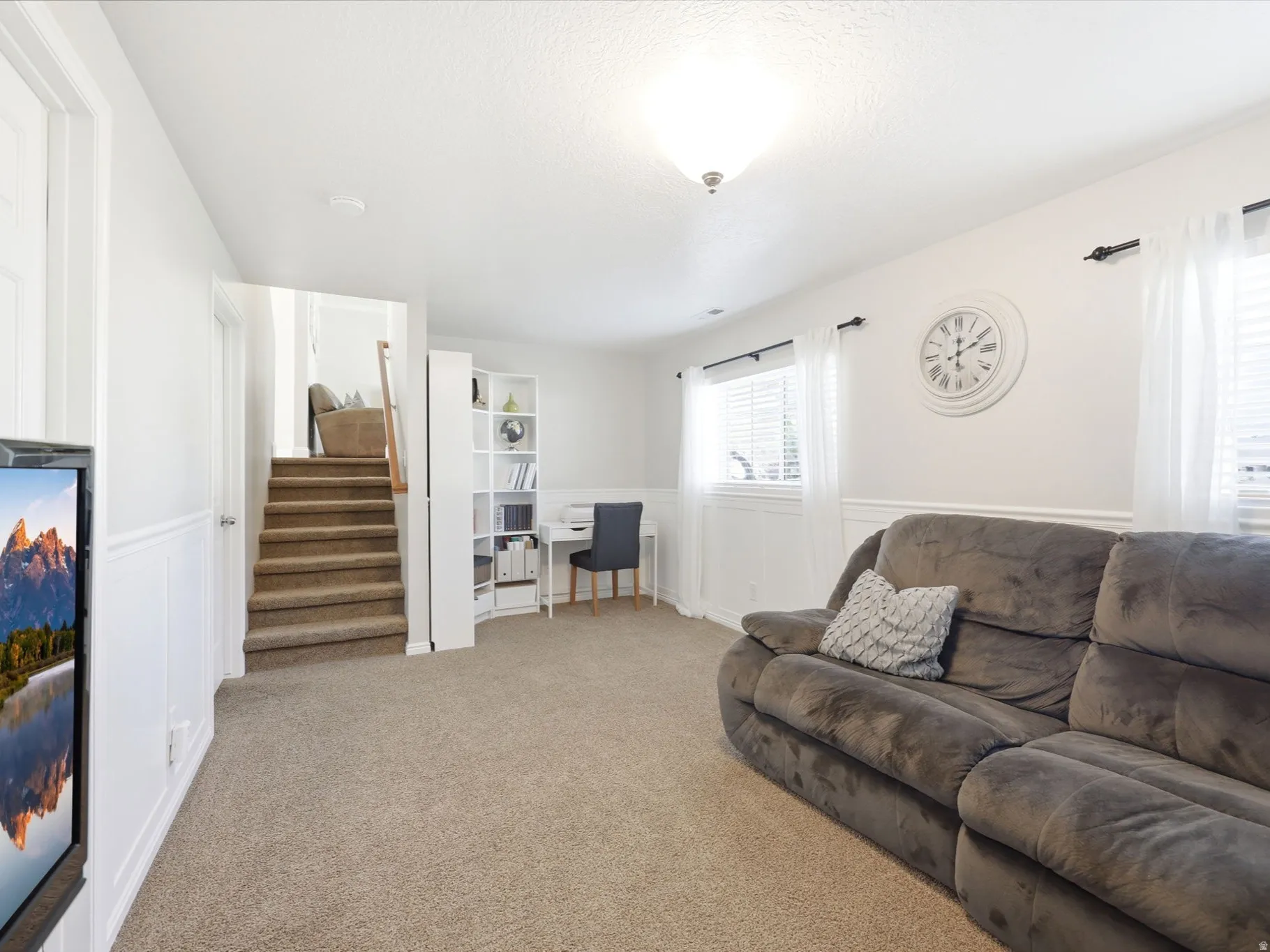 Spacious finished room featuring neutral carpet flooring, white wainscoting, and recessed windows with blinds
