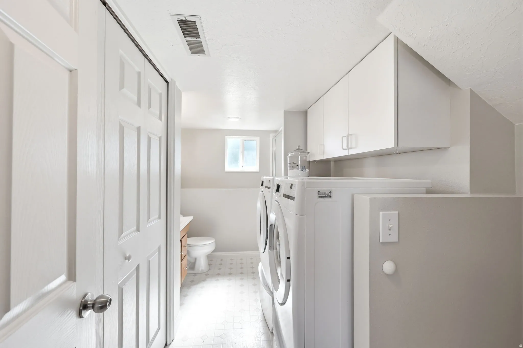 Dedicated laundry area featuring white upper cabinetry, light-toned walls, and patterned tile flooring