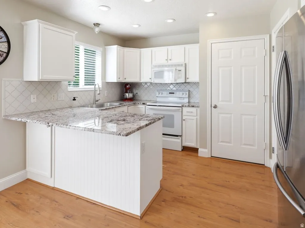 Kitchen featuring a central island with white beadboard paneling, light-toned granite countertops, white cabinetry, a subway tile backsplash, and wood-finish flooring
