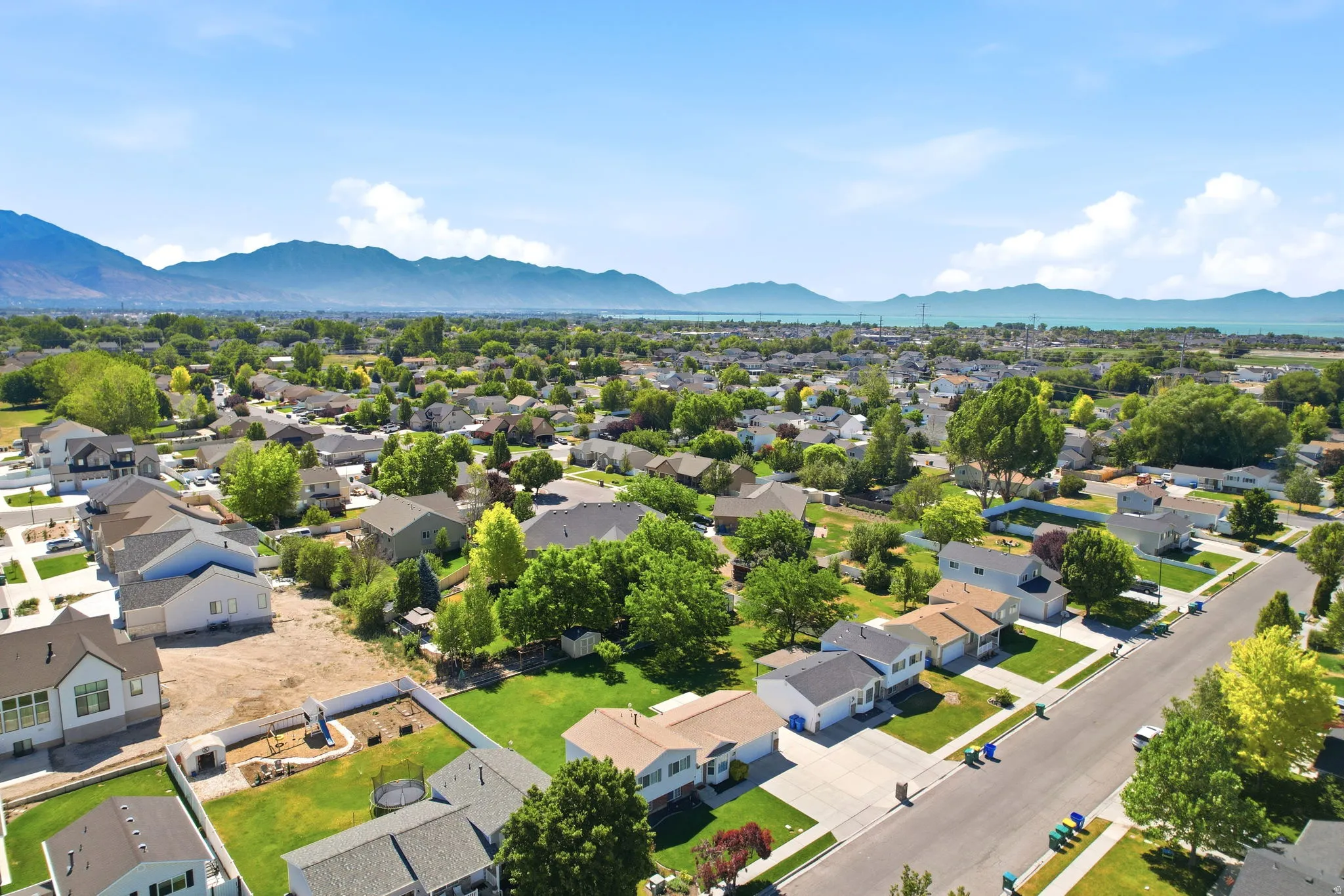 Expansive aerial perspective showcasing a residential neighborhood with a backdrop of distant mountains and a large body of water