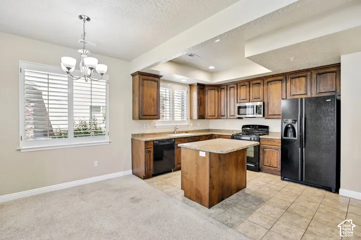 Kitchen featuring wood cabinetry, a central island with a solid surface countertop, black appliances, and tiled flooring