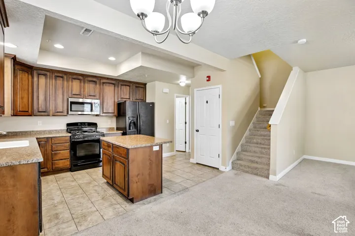 Kitchen featuring wood cabinetry, stainless steel microwave, black range, black refrigerator, and a central island with a countertop