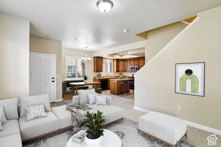 Open-concept living space featuring a carpeted area, a kitchen with wood cabinetry and stainless steel appliances, a dining area with built-in seating, and a staircase. Virtually staged.