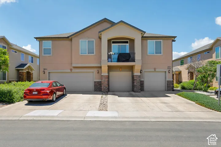 Duplex exterior featuring stucco siding, stone accents, and two single-car garages