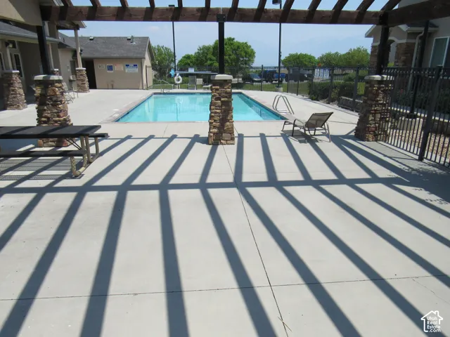 Outdoor swimming pool with concrete decking, surrounded by stone-clad columns supporting a pergola