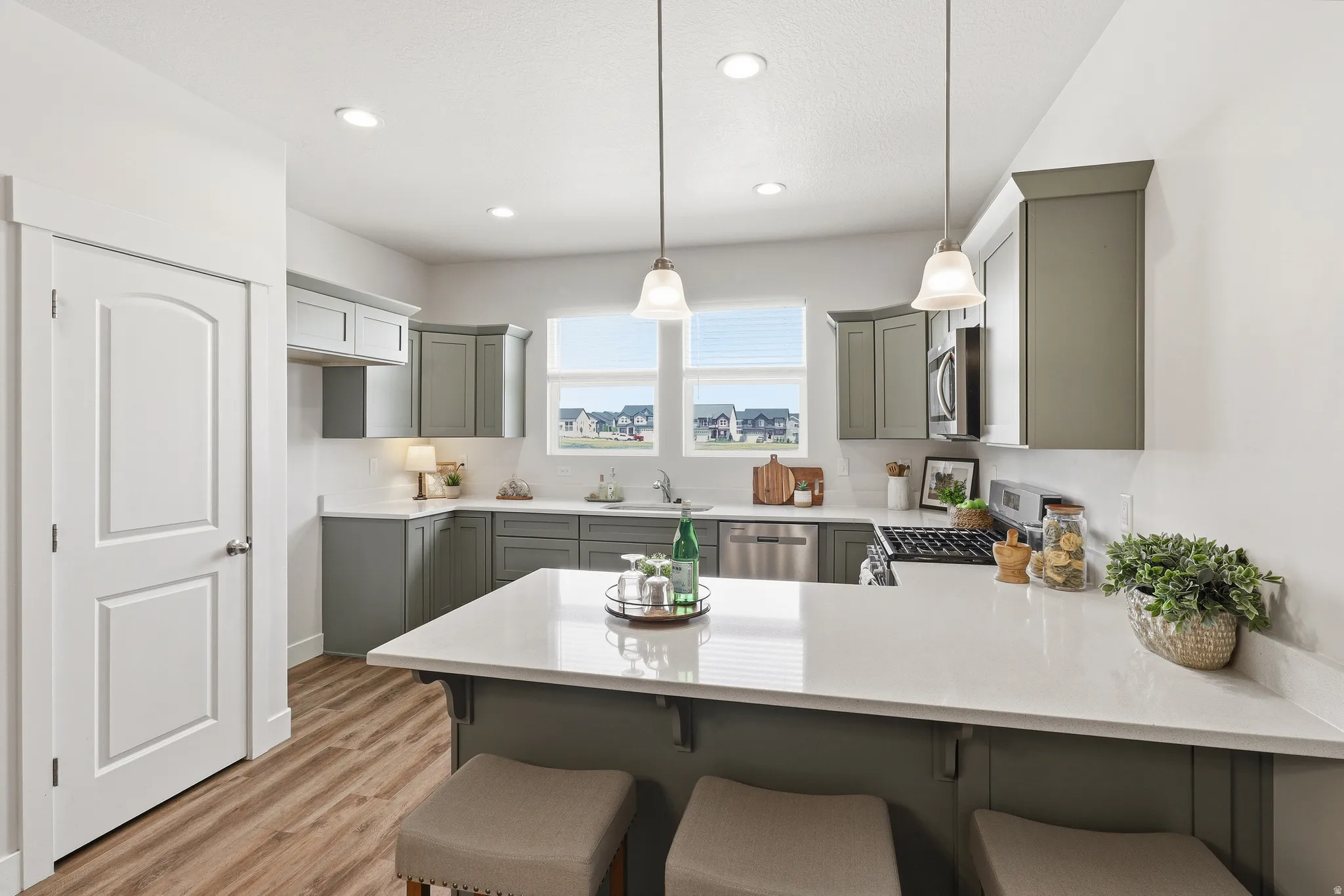 Modern kitchen featuring light green cabinetry, stainless steel appliances, white countertops, and wood-finish flooring