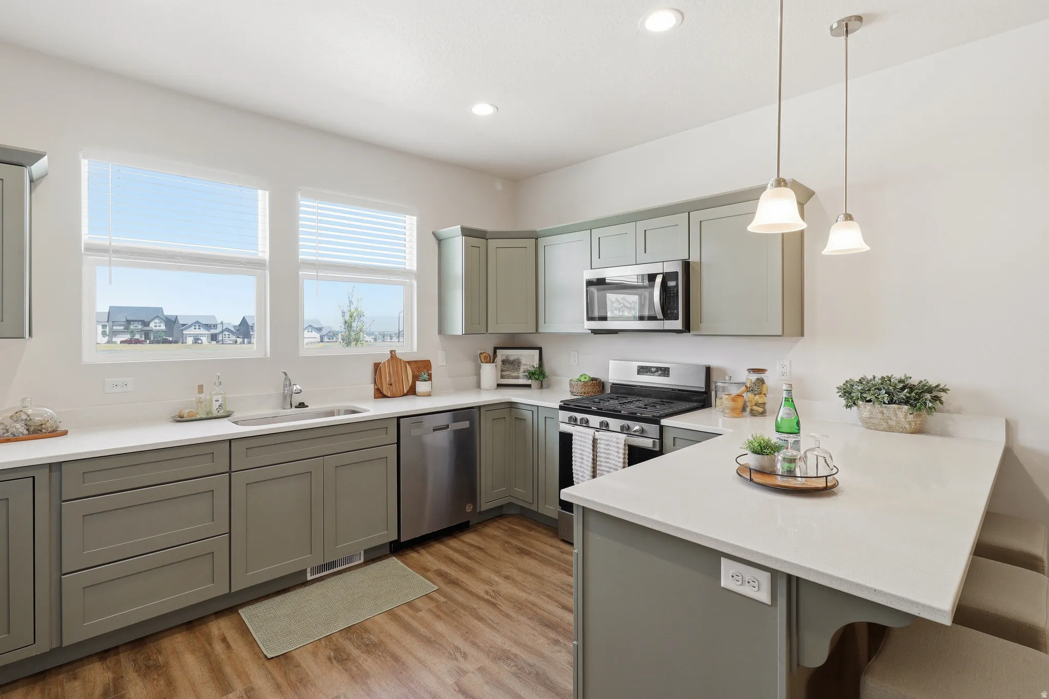 Open-concept kitchen featuring sage-toned cabinetry, light-toned countertops, and wood-finish flooring